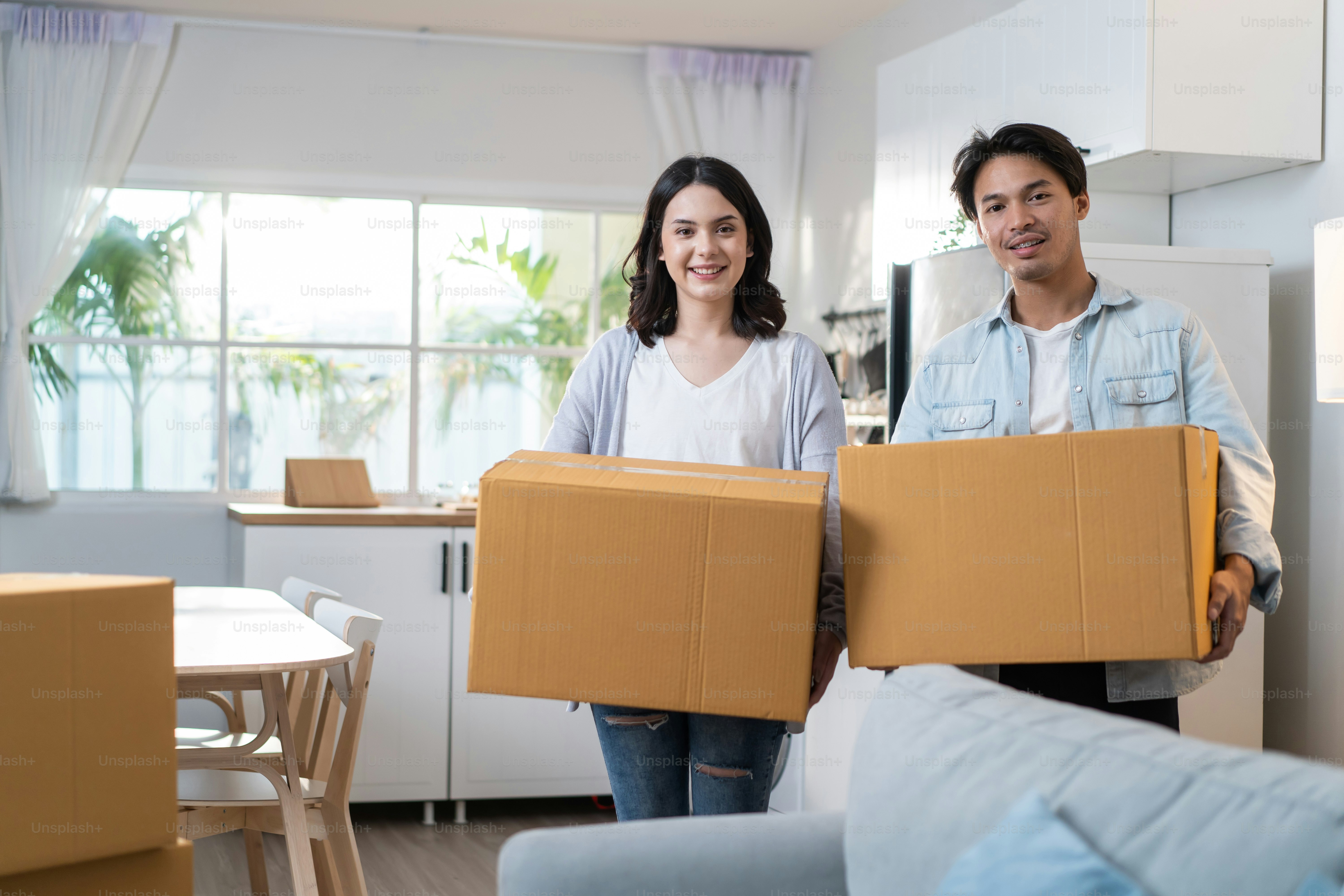 Asian young happy new marriage couple moving to new house together. Attractive romantic man and woman holding box parcel and suitcase with happiness and love. Family-Moving house relocation concept.