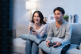 アジアの若い男性と女性のカップルは、家で一緒にゲームを楽しんでいます。魅力的で面白い男性と女性の友人は、リビングルームのソファに座って幸せを感じ、家で一緒にジョイスティックゲームをして時間を過ごします。