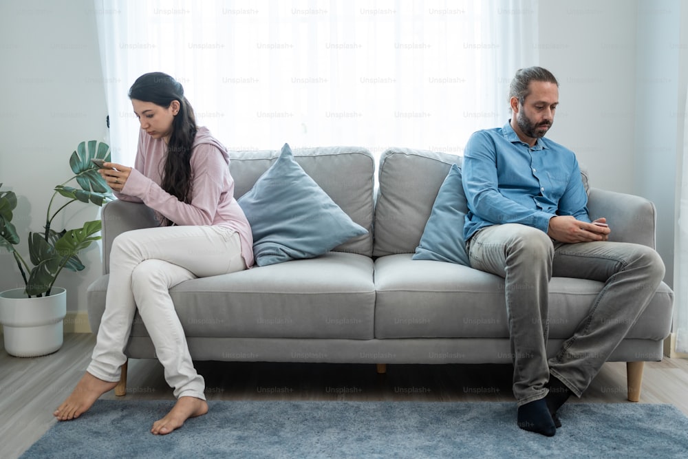 Caucasian phone addict couple don't pay attention with each other. Family problem, New marriage man and woman partner sit on sofa and using smartphone, ignore husband and wife in living room at home.
