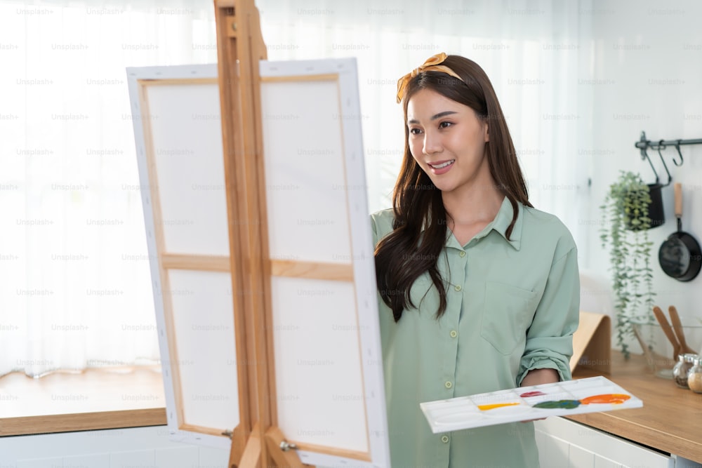 Giovane artista donna di talento asiatica che colora sulla tavola di pittura in casa. Attraente bella immagine femminile disegna arte, creando opere d'arte con vernice ad acquerello e pennello godere di attività di creatività a casa.