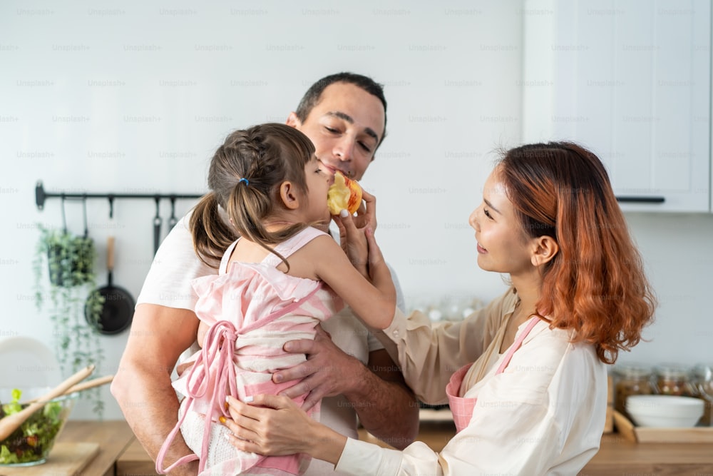 Asian beautiful young mother cooking foods with baby kid in kitchen. Happy family spend time on holiday together in house, loving parent tying apron for little child daughter prepare to make breakfast