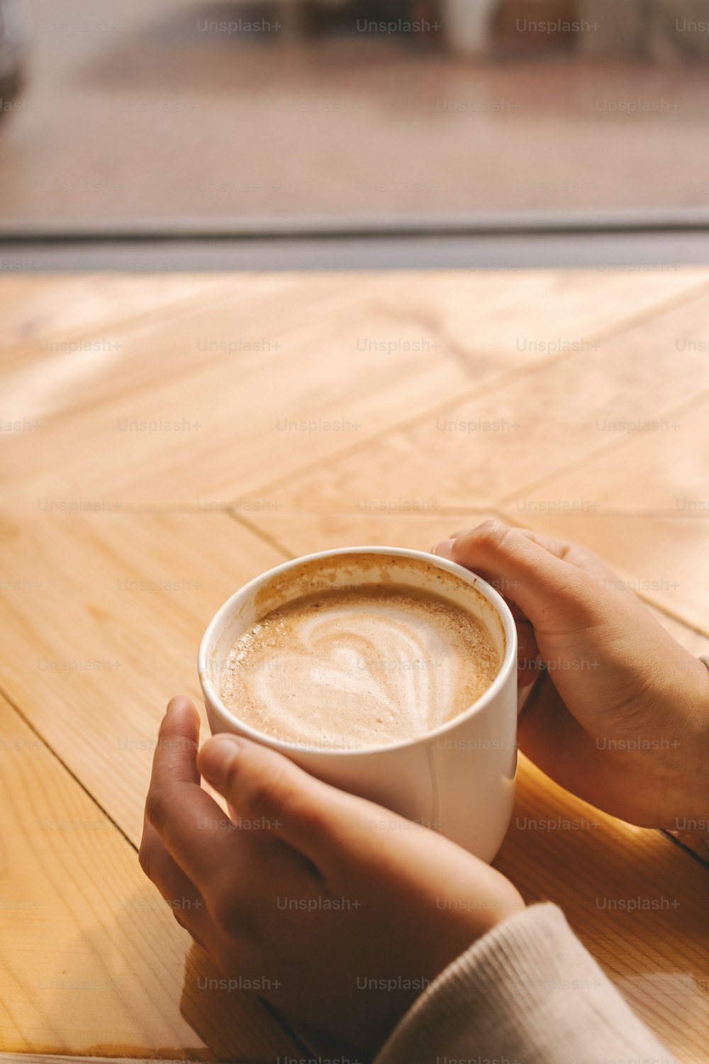 Una persona sosteniendo una taza de café encima de una mesa de madera