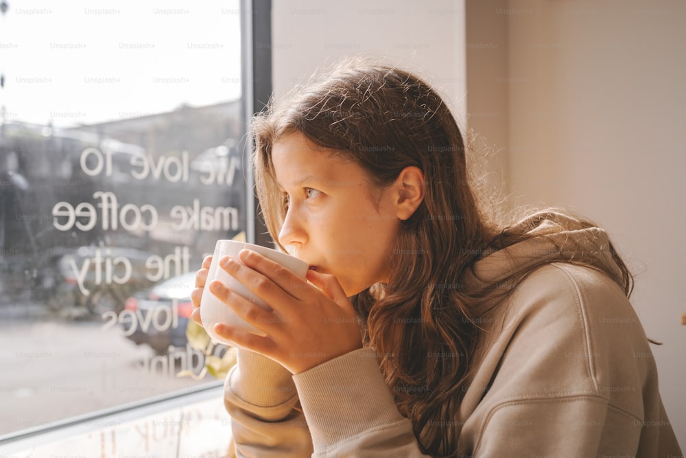 Une fille buvant une tasse de café devant une fenêtre