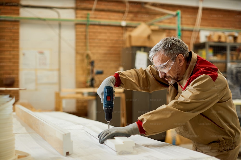 Lavoratore maschio che usa un trapano mentre fa mobili in un laboratorio di falegnameria.