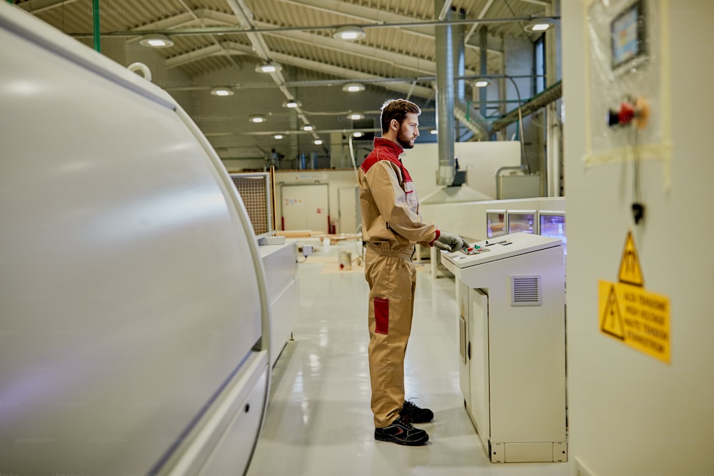 Male industrial worker operating automated machine for wood processing in a factory.