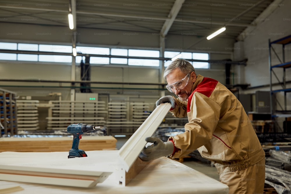 Feliz carpintero adulto medio analizando una pieza de madera mientras trabaja en un taller.