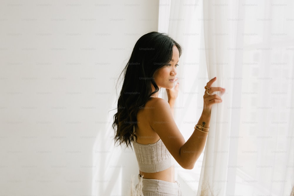 a woman standing in front of a window holding a cell phone to her ear