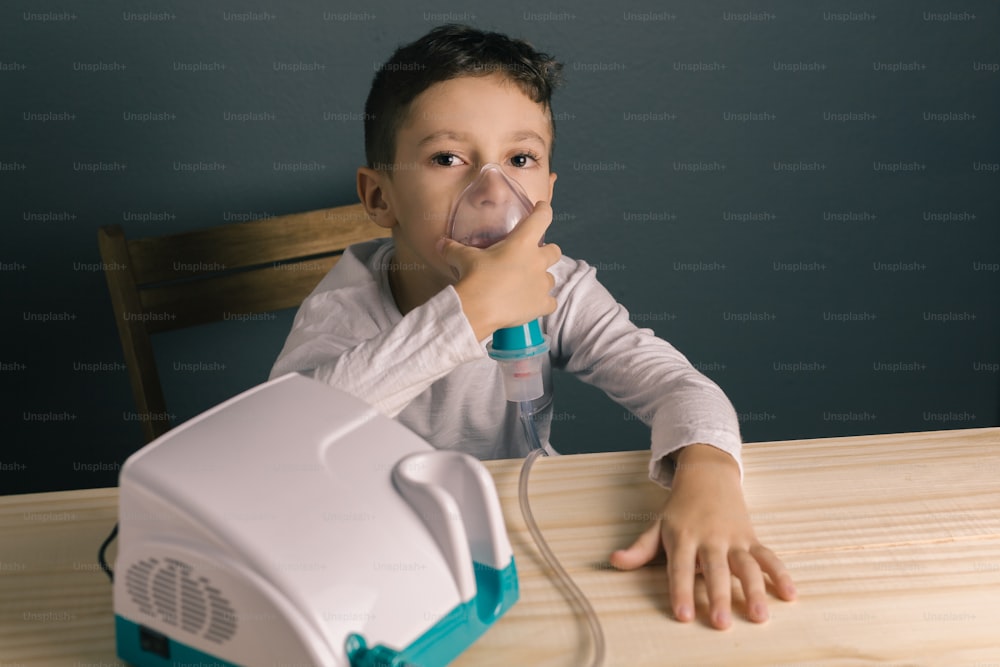 Beautiful sick boy inhalation therapy by the mask of inhaler. Image of a cute kid with respiratory problem or asthma. View of nebulizer with smoke from oxygen mask.