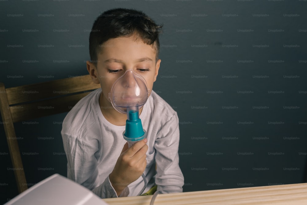 Beautiful sick boy inhalation therapy by the mask of inhaler. Image of a cute kid with respiratory problem or asthma. View of nebulizer with smoke from oxygen mask.
