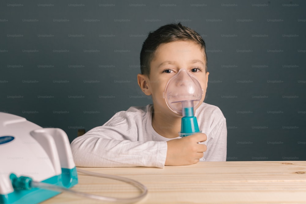 Hermosa terapia de inhalación de niño enfermo por la máscara del inhalador. Imagen de un niño lindo con problema respiratorio o asma. Vista del nebulizador con el humo de la máscara de oxígeno.