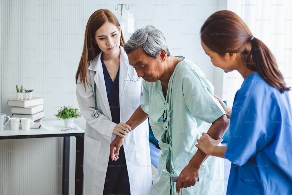 Asian doctor woman and nurse encourage disabled old man patient sitting on bed at hospital, asian medical concept