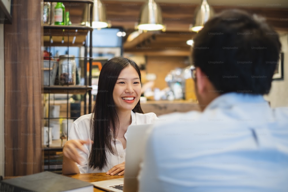 Junge schöne asiatische Geschäftsfrau im Café, diskutiert Geschäfte während des Interviews mit jungem Geschäftsmann
