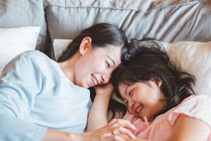 Asian mother kissing daughter in bedroom, with love and warm family concept