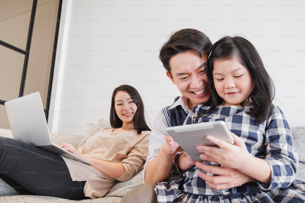 Família asiática feliz que passa o tempo juntos em casa jogando jogo, tablet para a educação
