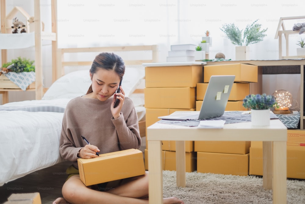 オンラインビジネス、オンラインショッピング、配送、箱とパッケージのコンセプトのための顧客と電話を話す若いアジアの女性の売り手。