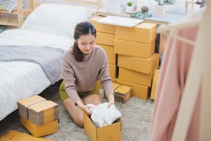 Junge asiatische Verkäuferin verpackt Kleidung Produkt für Online-Business, Online-Shopping, Versandkarton und Paket