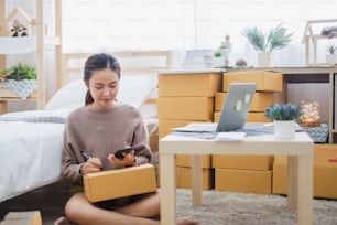 Young asian woman seller talking phone with customer for online business, online shopping, shipping, box and package concept.