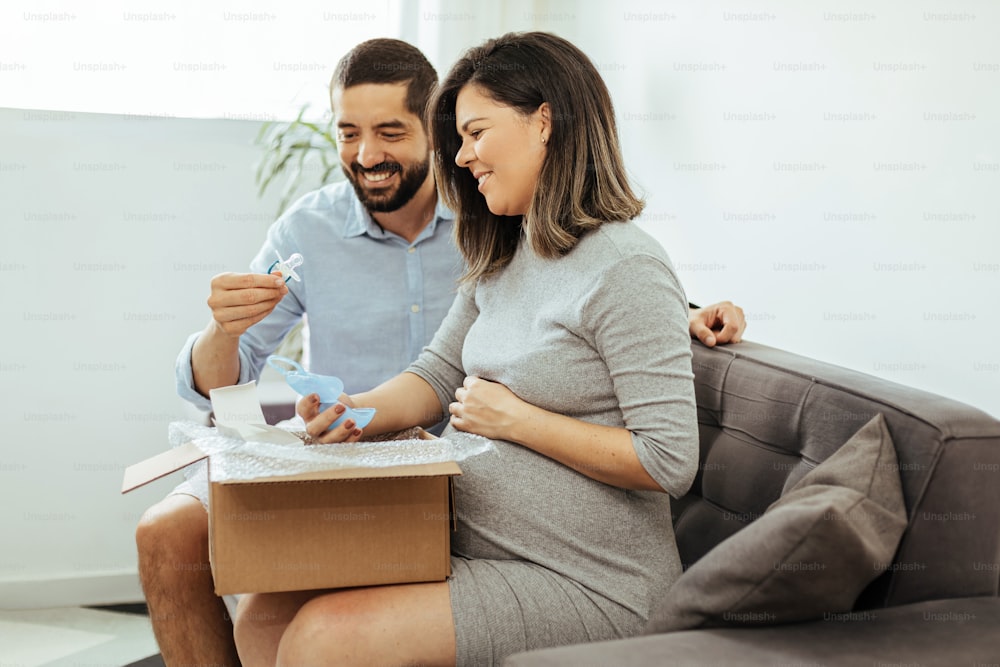 Couple adulte attendant bébé déballant des articles pour bébé achetés en ligne.