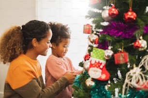 Mãe africana negra e sua filha fofa decorando árvore de Natal para o Natal e feliz novo conceito