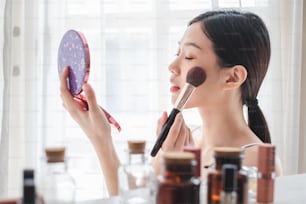 Jovem mulher asiática bonita aplicando cosméticos maquiagem em seu rosto, cuidados de saúde beleza da pele e conceito de maquiagem