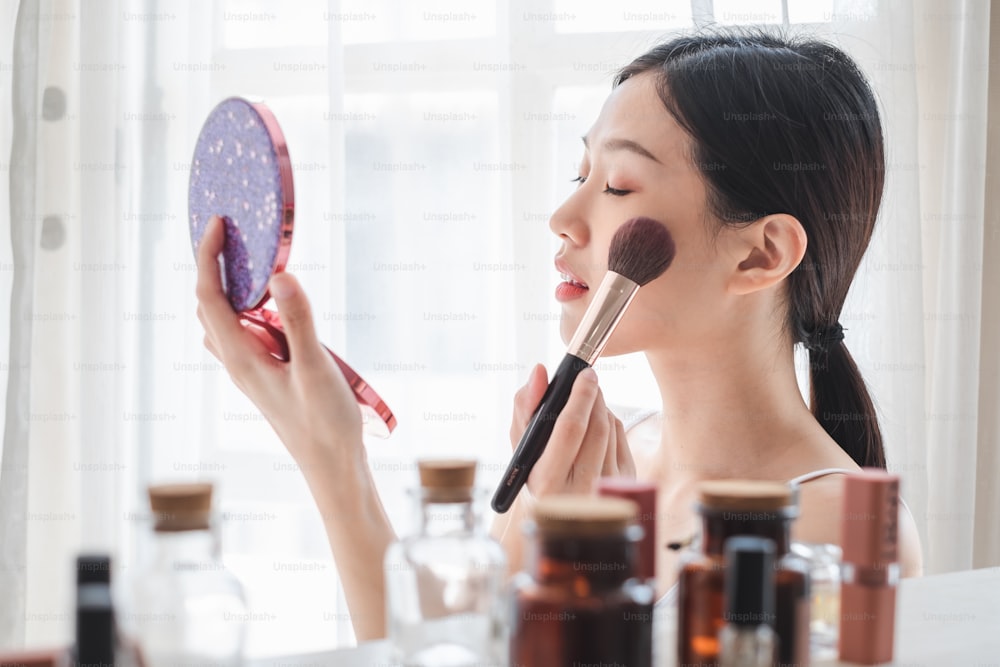 Young beautiful Asian woman applying cosmetics make up on her face, health beauty skin care and make up concept