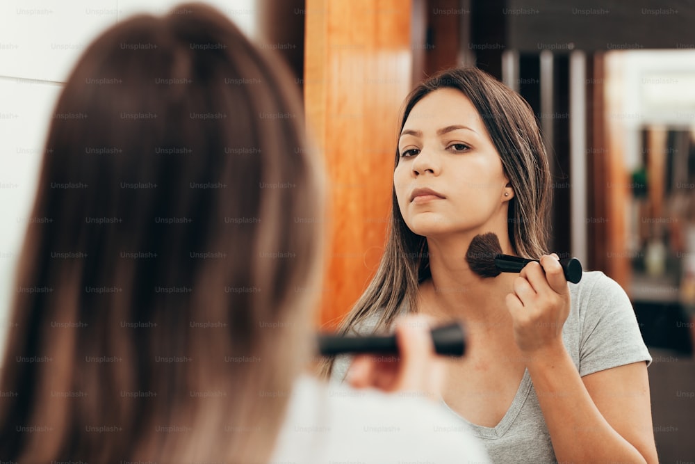 スキンケア。鏡の前でブラシで化粧をする女性