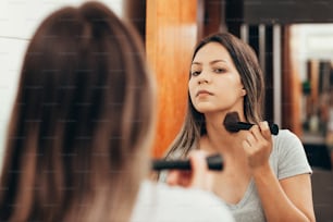 Skin care. Woman applying make-up with brush in front of mirror