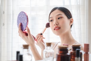Jovem mulher asiática bonita aplicando cosméticos maquiagem em seu rosto, cuidados de saúde beleza da pele e conceito de maquiagem