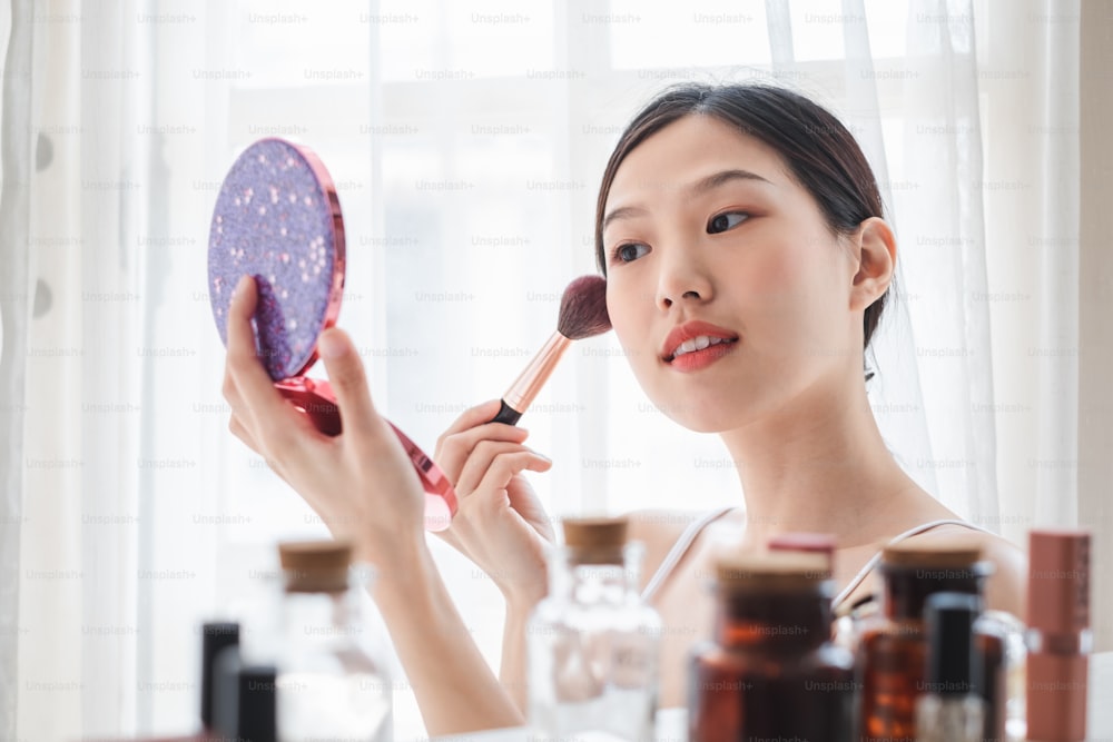 Young beautiful Asian woman applying cosmetics make up on her face, health beauty skin care and make up concept
