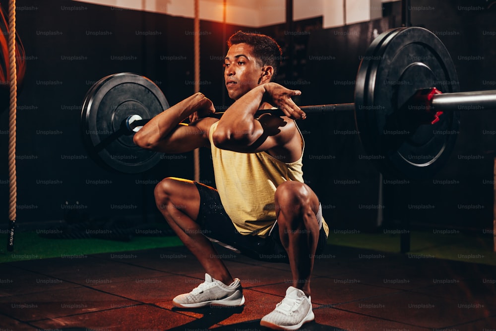 Hombre musculoso en el gimnasio haciendo ejercicios de peso pesado. Joven haciendo levantamiento de pesas en el club de salud