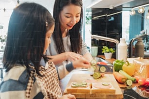 Asian Mother and her daughter kid cooking food for breakfast in kitchen