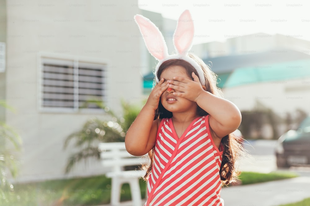 Cute little girl with bunny ears and basket of Easter eggs in the garden. Easter egg hunt