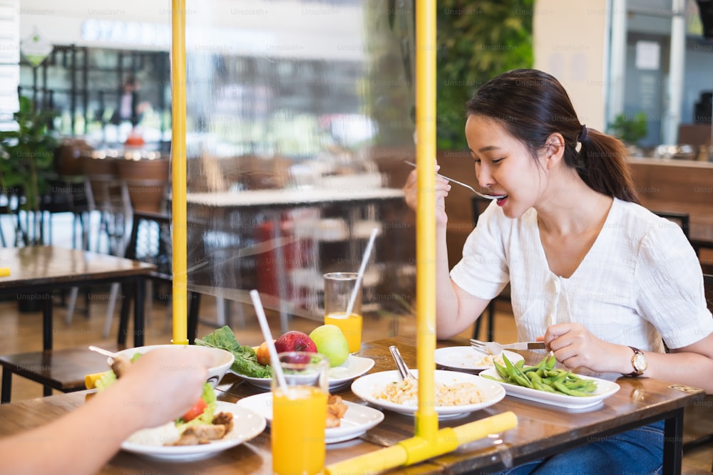 Donna asiatica seduta nel ristorante che mangia cibo con scudo da tavola per proteggere l'infezione da coronavirus covid-19, ristorante e concetto di distanziamento sociale