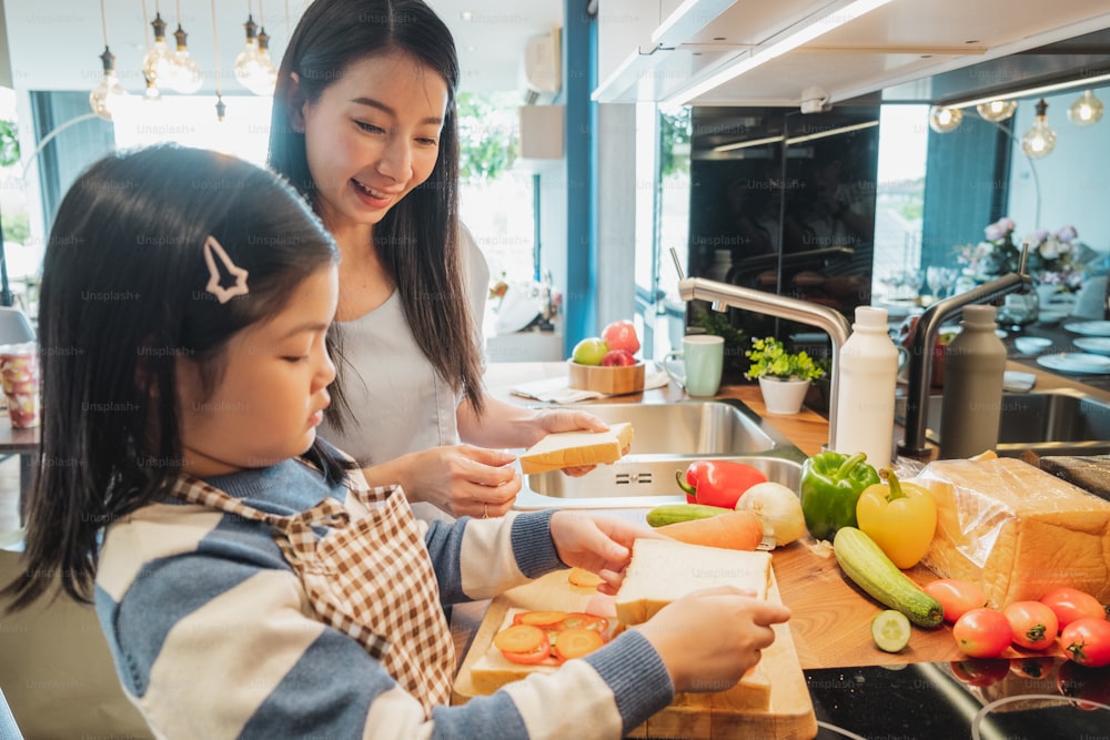 Asian Mother and her daughter kid cooking food for breakfast in kitchen
