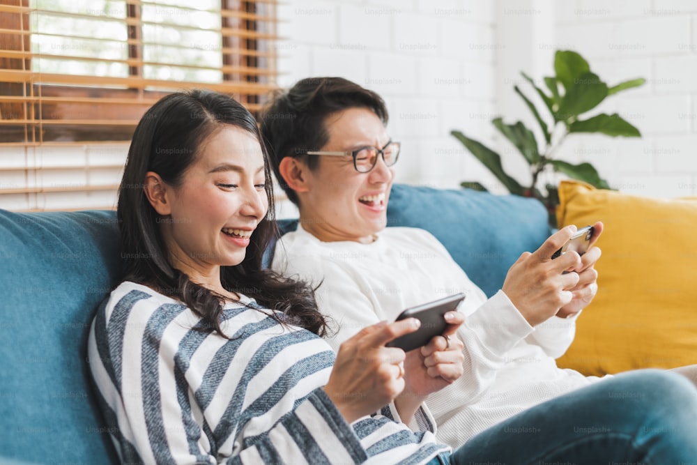 Lifestyle Asian couple man and woman playing game on mobile phone together at home, Asian couple family lifestyle concept