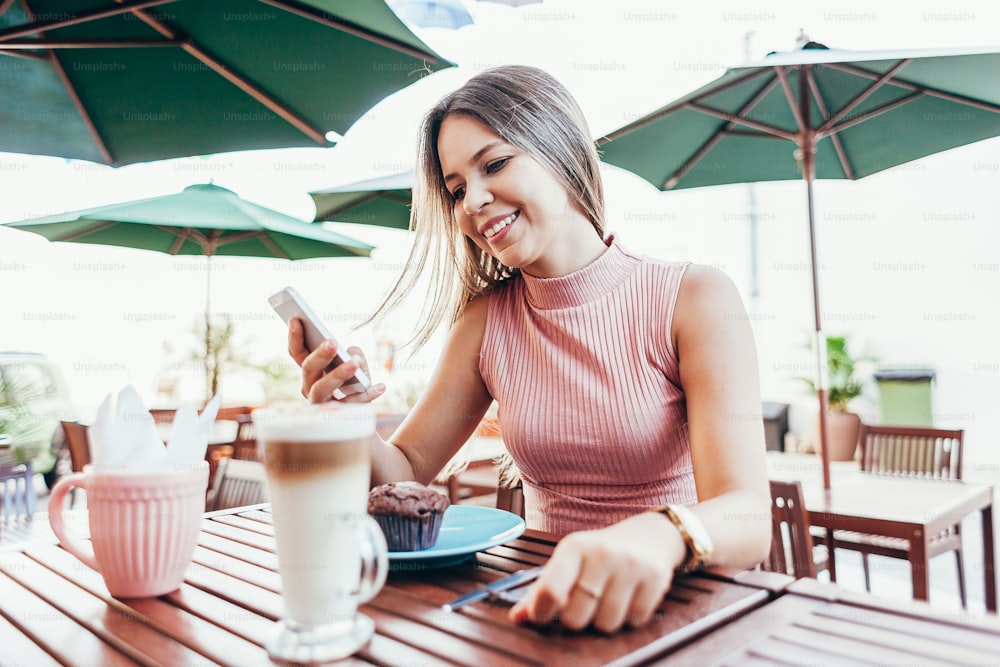 Junge Frau frühstückt mit Kaffee und Kuchen draußen in einem Café