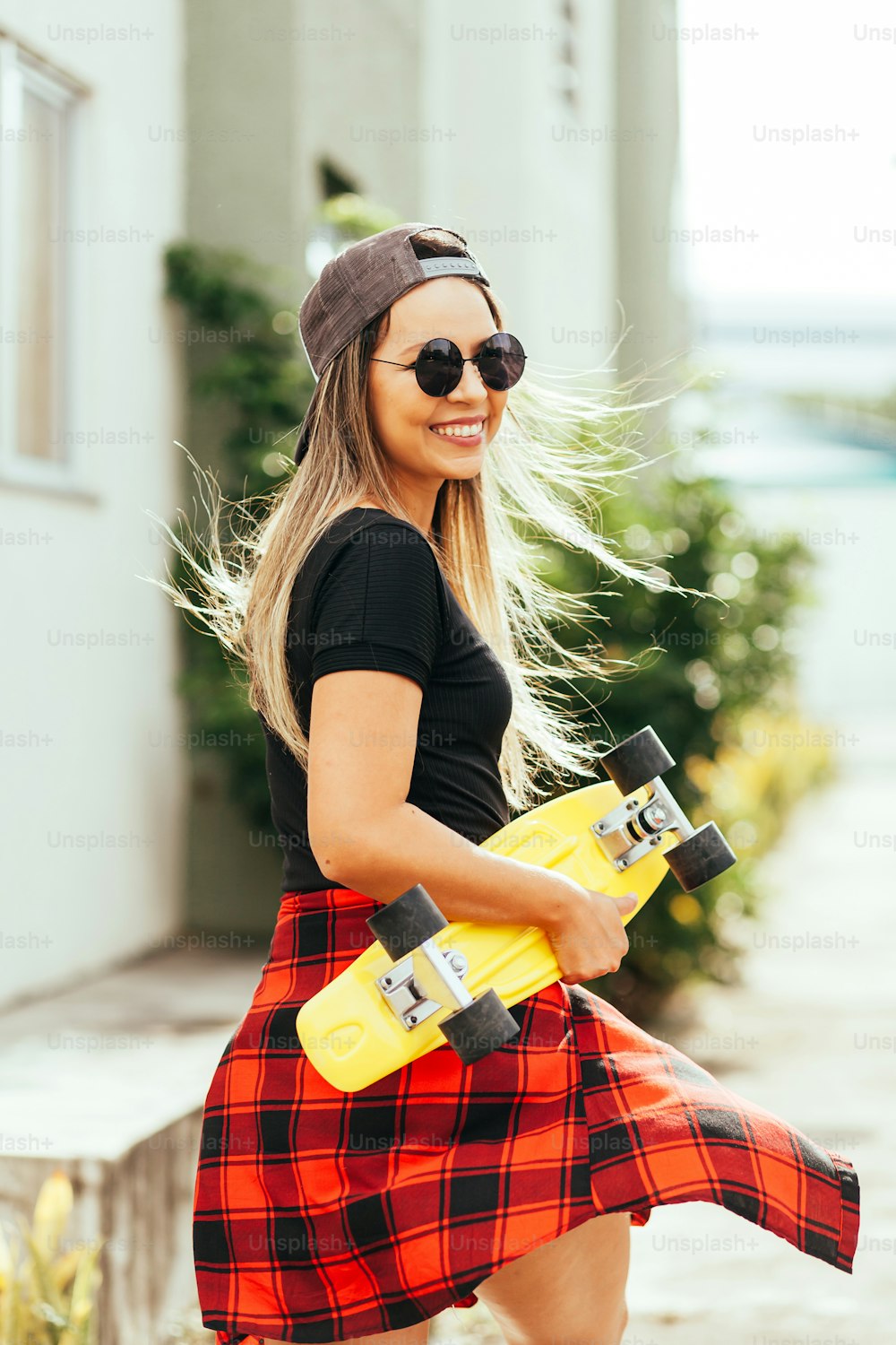 Young positive woman carrying skateboard in the city