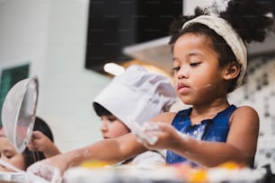 キッチンでケーキベーカリーを作るグループの多様性の子供の女の子
