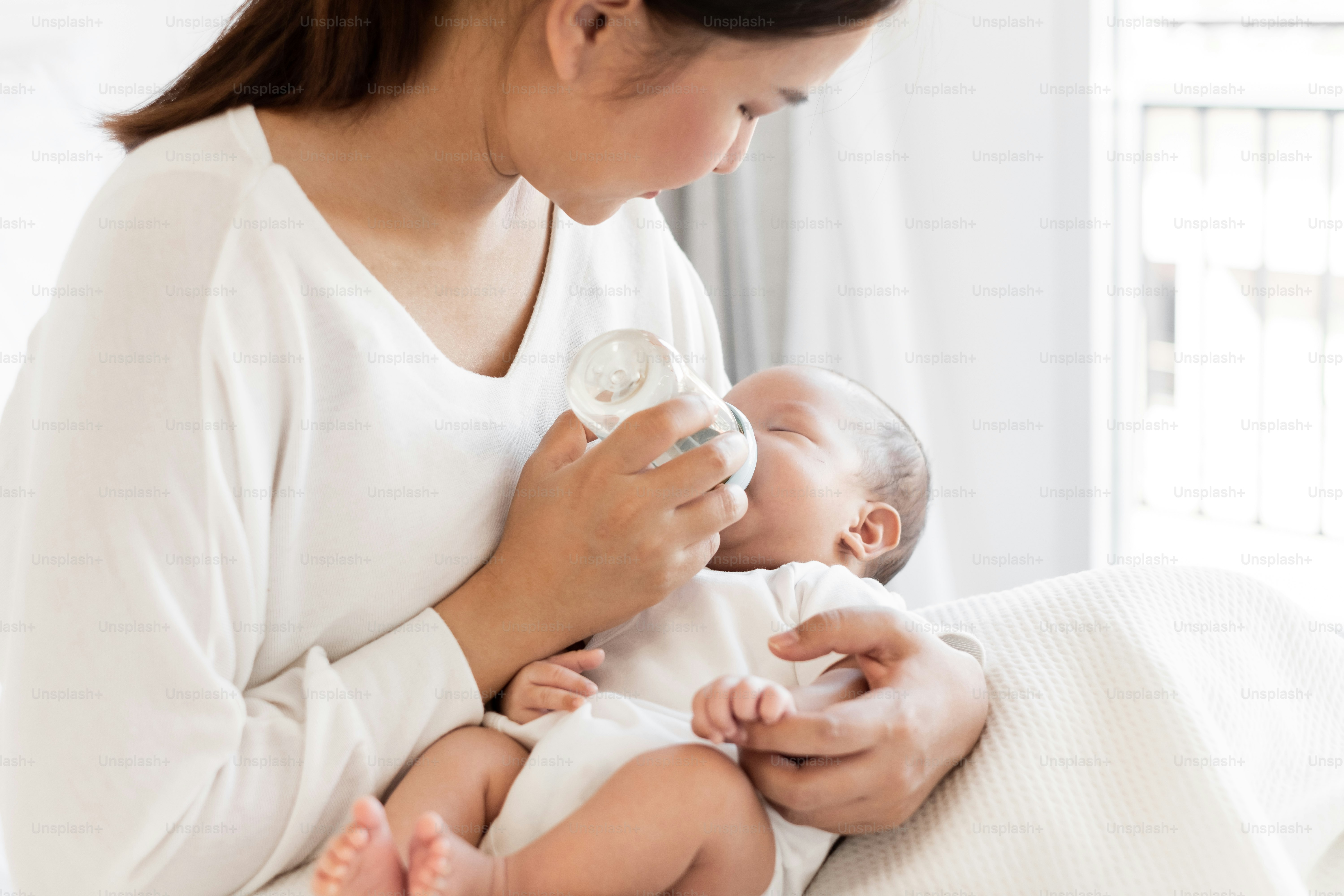 Mother breast feeding milk to Asian newborn baby on white bed
