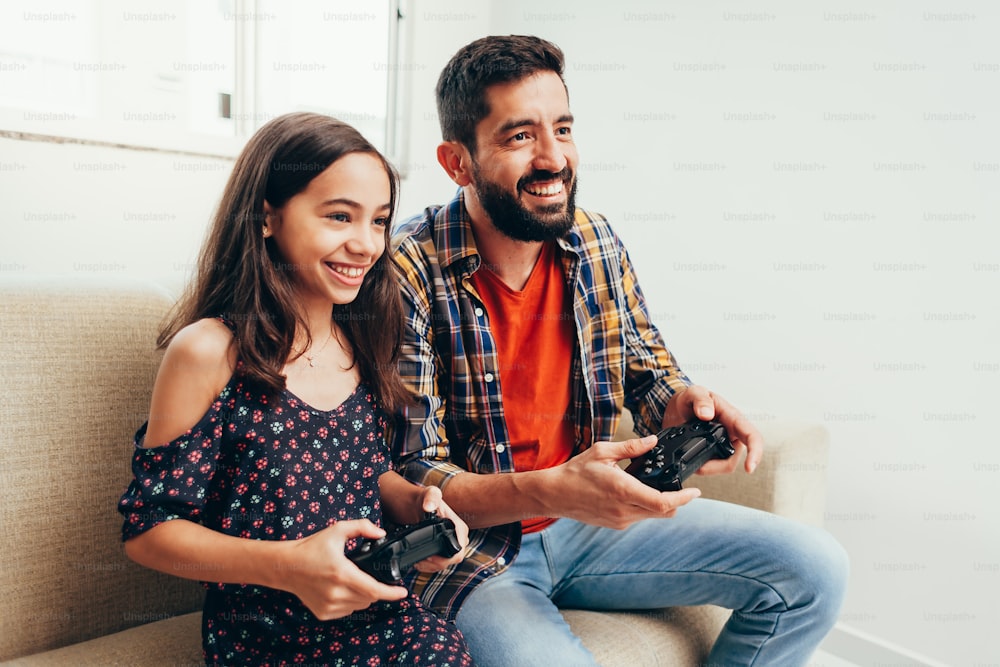 Padre e hija sonrientes jugando videojuegos en casa