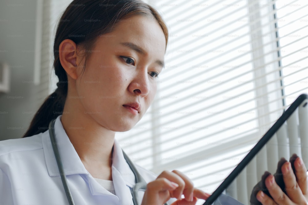 Asian woman doctor reading medical report on tablet, working in medical office hospital