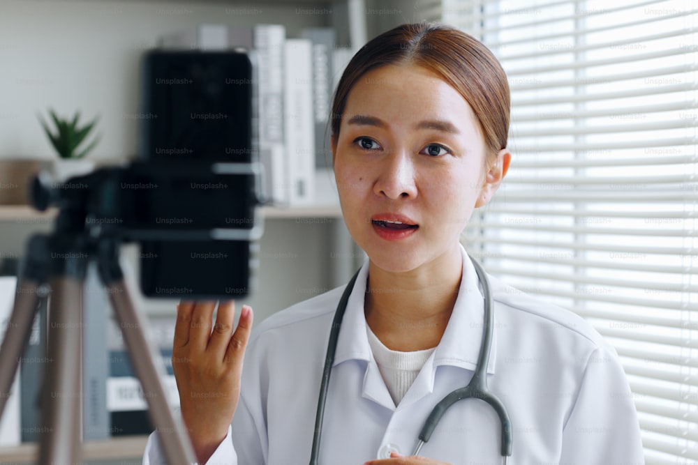 Asian woman doctor making online live streaming broadcast talking over camera recording in hospital, medical and healthcare blogger, vlogger concept