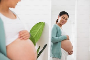 Asiatische schwangere Frau, die mit dickem Bauch zu Hause spiegeln möchte