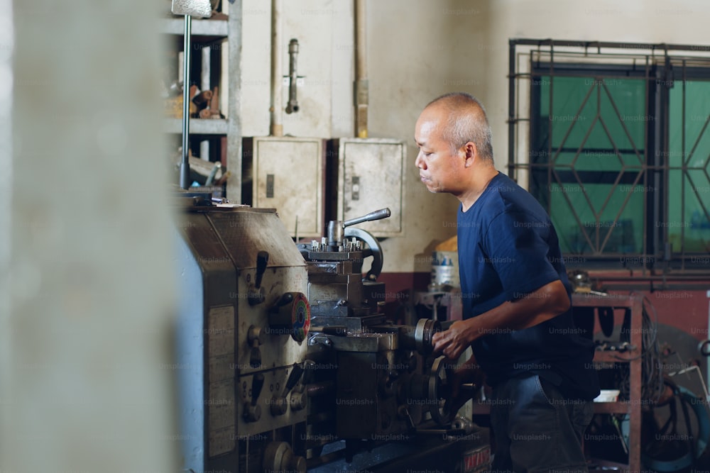 Technician asia worker using turning lathe machine for metalworking in workshop factory