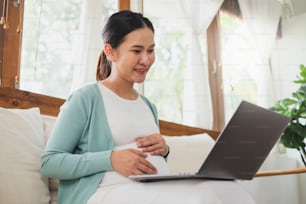 Asiatische schwangere Frau, die Laptop zu Hause benutzt