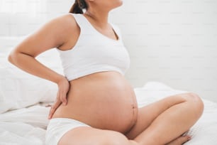 大きなお腹を持つアジアの若い妊婦は腰痛、ベッドの上で背中の痛みを持っています