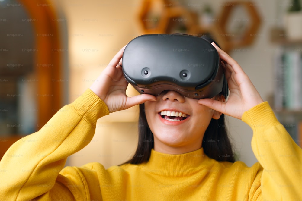 Young Asian woman feeling excited while using 360 VR headset for virtual reality/ metaverse at home