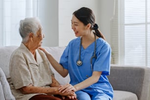 Junge asiatische Krankenschwester, Pflegekraft, Pflegerin eines Pflegeheims muntert eine ältere asiatische Frau zu Hause auf