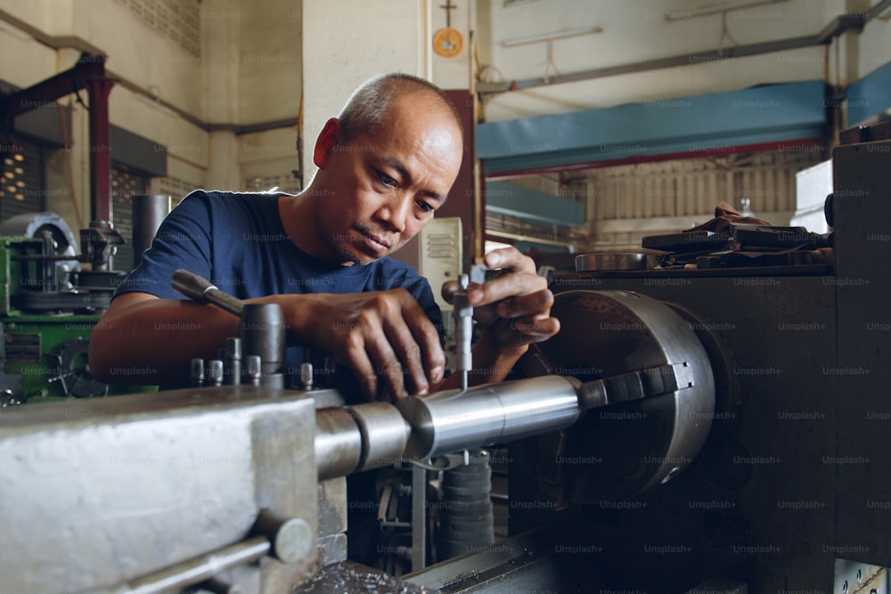 Technician asia worker using vernier caliper measure detail of workpiece for checking size in workshop lathe machine factory