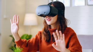 Jovem asiática que se sente animada ao usar o fone de ouvido 360 VR para realidade virtual / metaverso em casa
